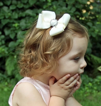 little girl wearing special occasion pink tulle dress and ivory hair bow with a pearl and rhinestone center